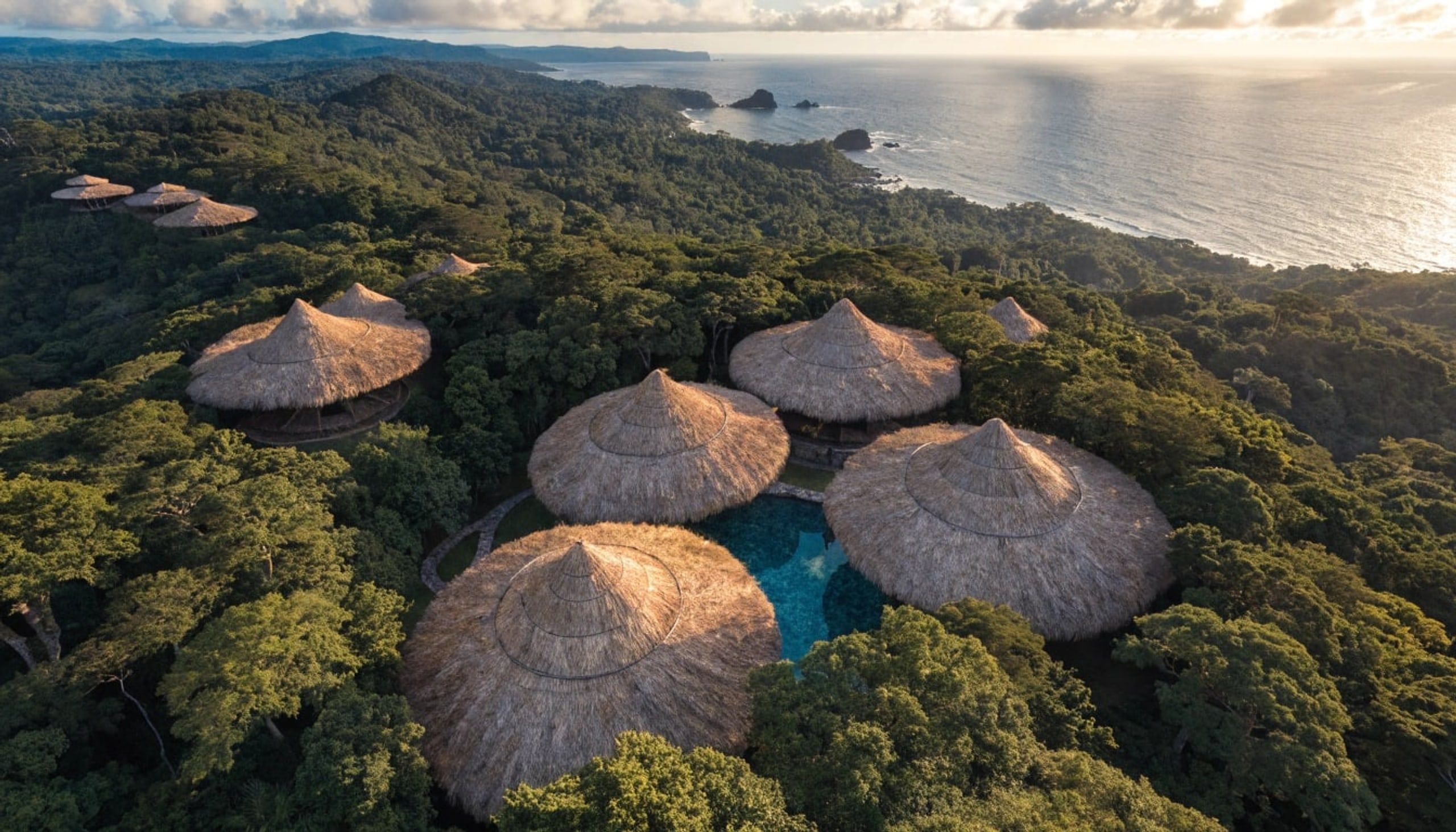 Mid-altitude aerial showing a tight cluster of round bamboo cabins around a small pool.