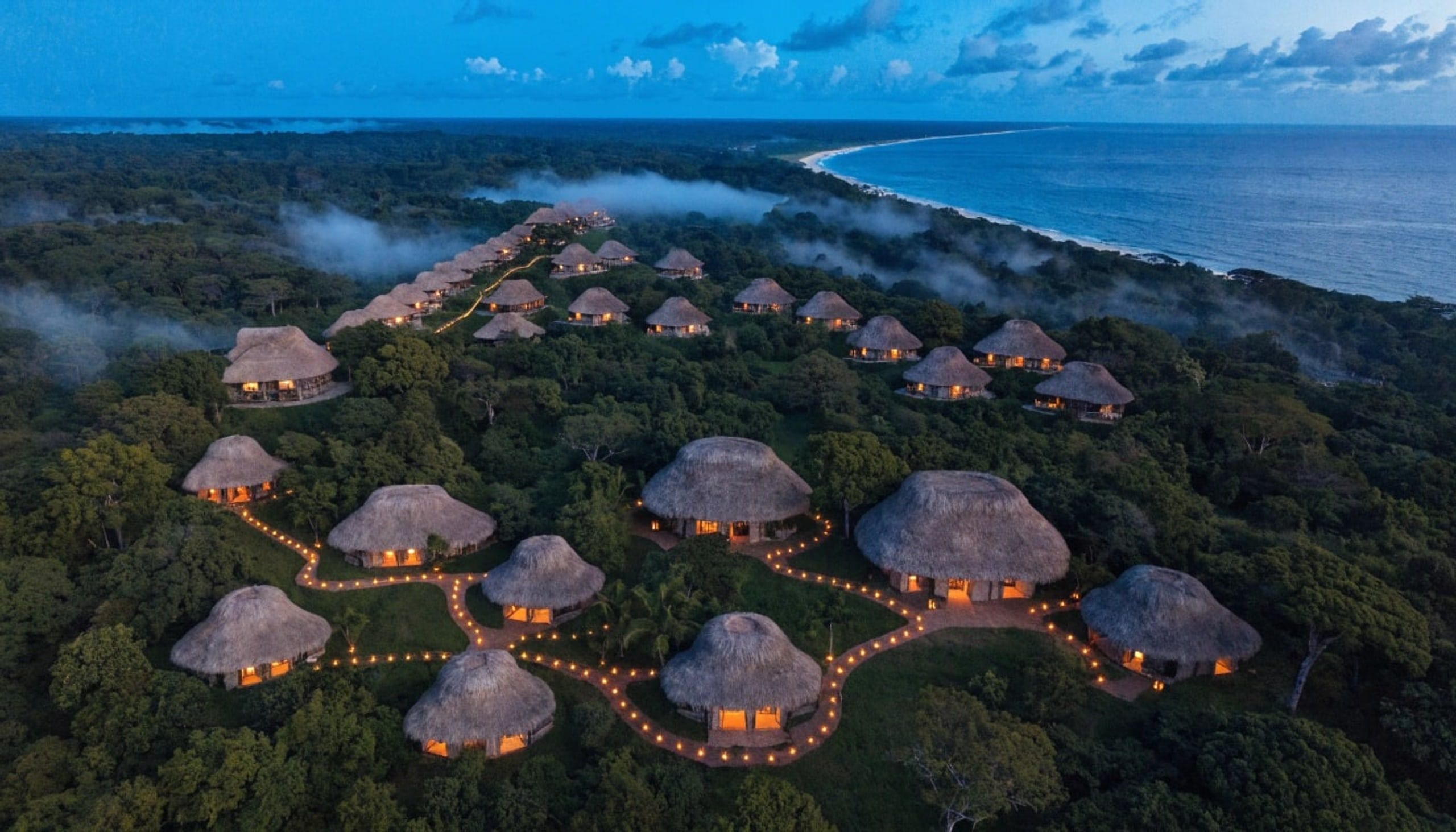 Aerial view of the bamboo retreat at dusk, cabin lights threaded through the canopy.